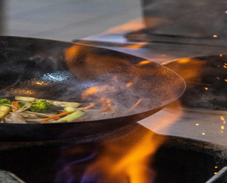 Vegetables searing in a wok over open flame at Textures