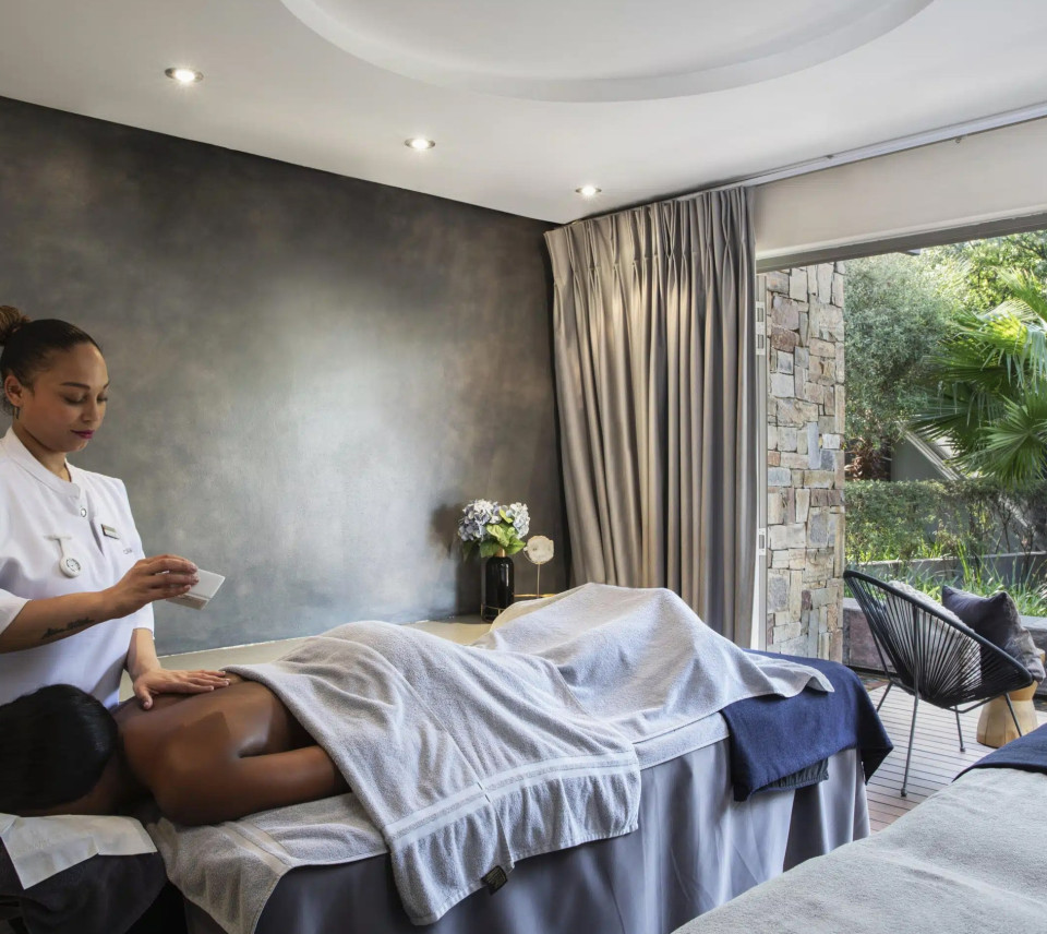 A therapist preparing a treatment bed in a Camelot Spa treatment room opening onto a garden